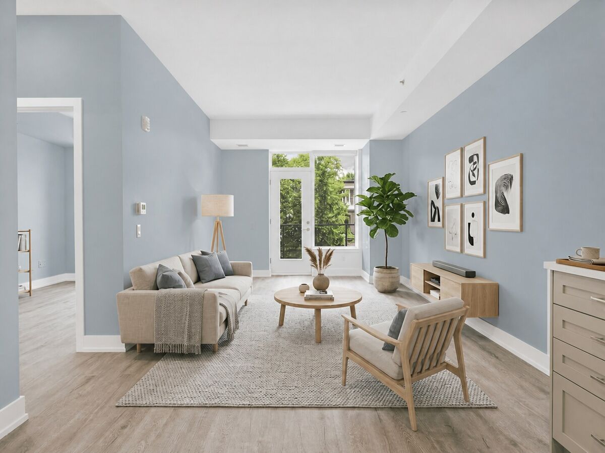 After: the same living room with dusty blue walls. The sofa, rug, round table, armchair, plant and prints are unchanged.
